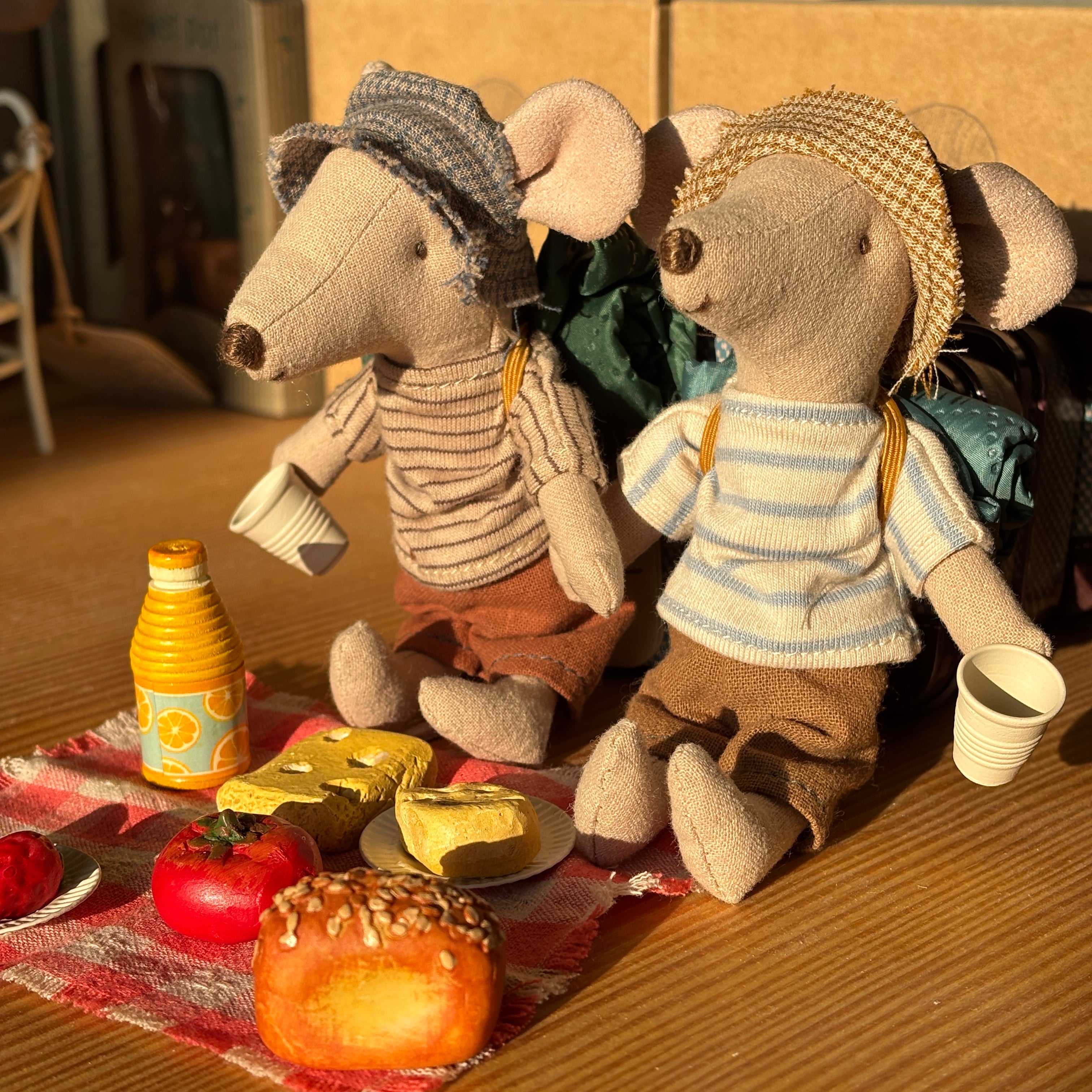 Two toy mice with accessories on a table with food items.